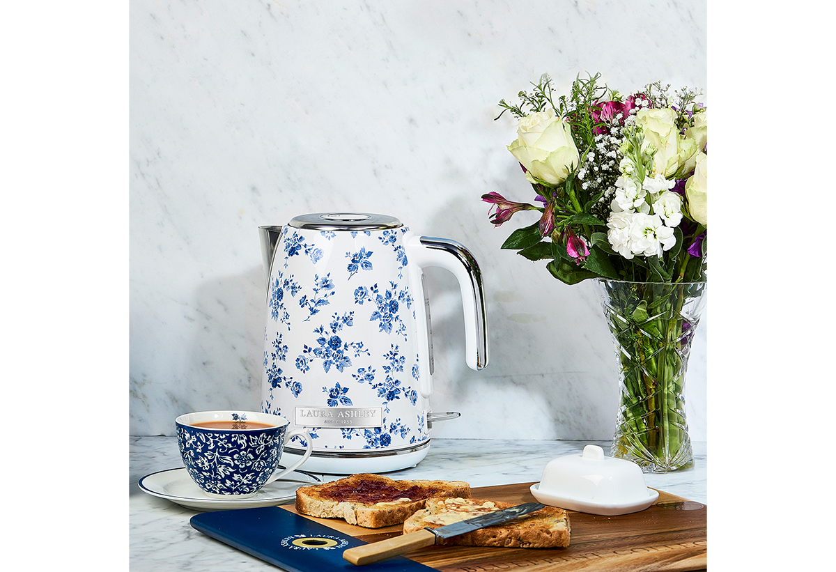 Απεικονίζονται σε ένα τραπέζι ο βραστήρας μαζί με ένα φλιτζάνι καφέ και 2 φέτες ψωμί με μαρμελάδα.